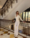 A woman posing in a white long-sleeve zip-up top and matching white wide-leg pants, accessorized with sunglasses.